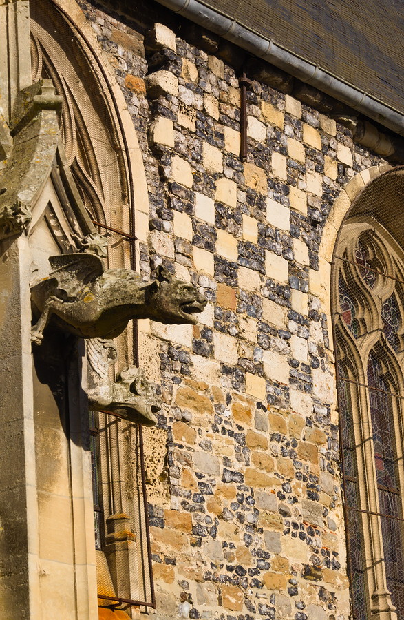 Détail de la façade de l'église : gargouille ailée, pierres en damier et aperçu des vitraux