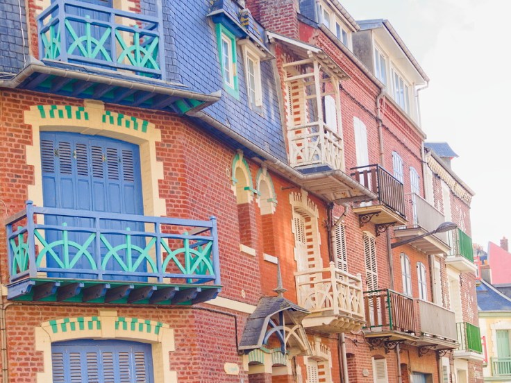 Détail d'une façade de villa, contraste entre briques rouges et volets et balcons bleus.