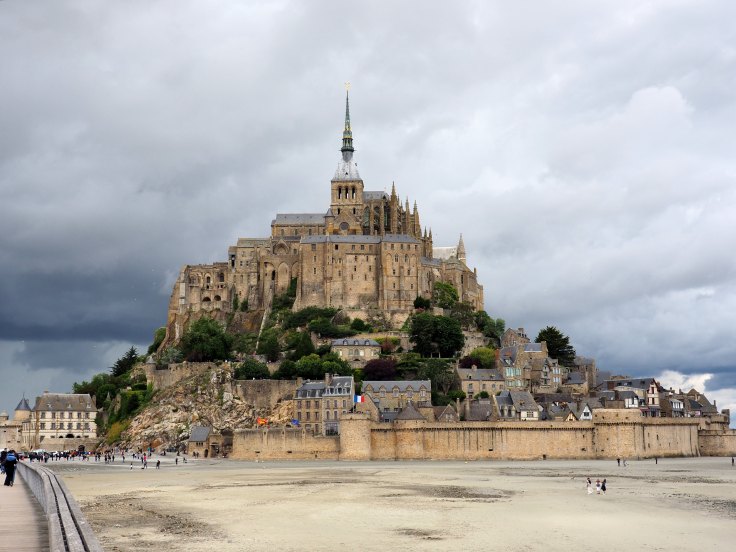 Mont Saint-Michel et sa route d'accès sur fond de ciel orageux, à marée basse