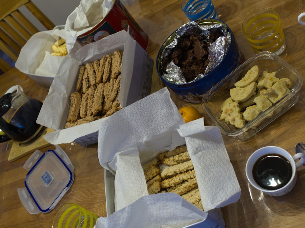 6 boîtes remplies de biscuits de Noël sur table avec tasse et cafetière pleines.