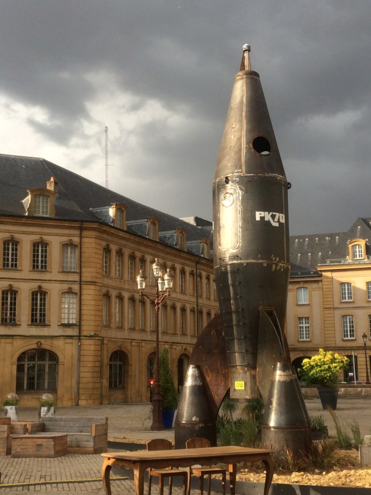 Fusée posée devant bâtiment classique, ciel tourmenté.